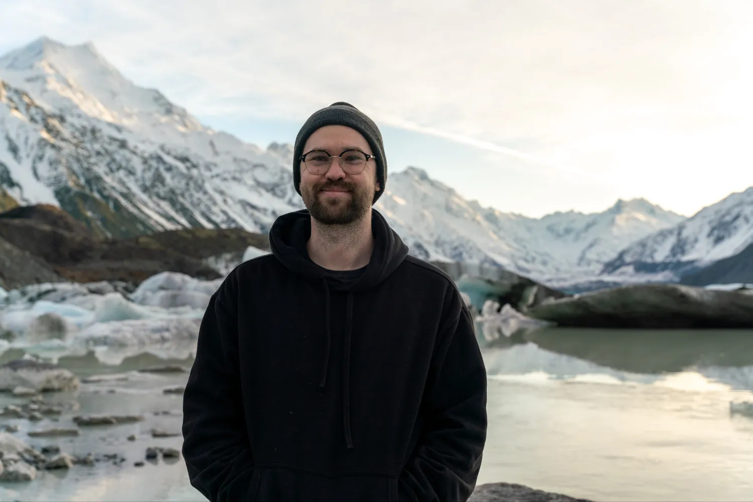 Mitchell Henderson standing in front of snow-capped mountains and a glacier lake