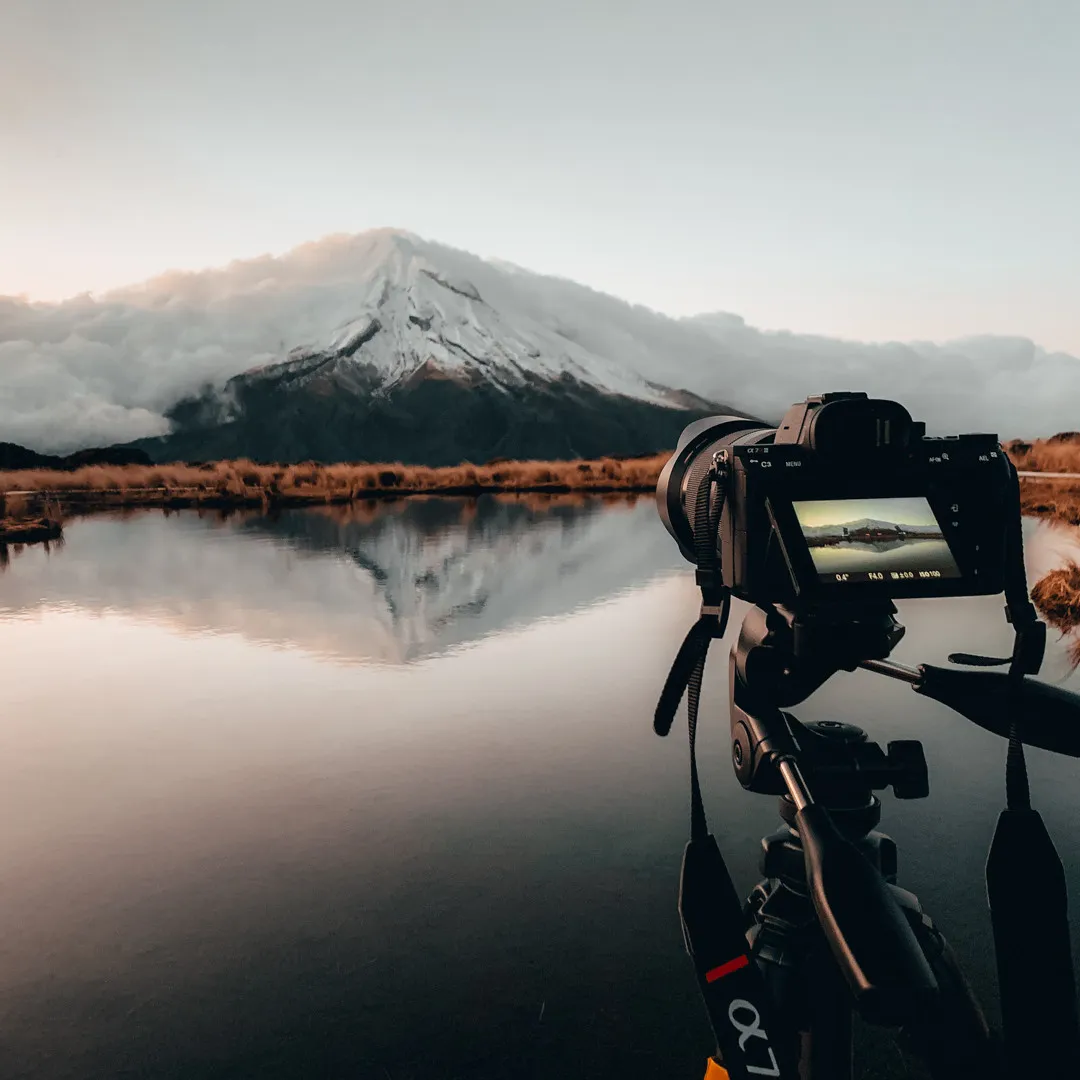 Camera on a tripod photographing Mount Taranaki reflected in a tarn